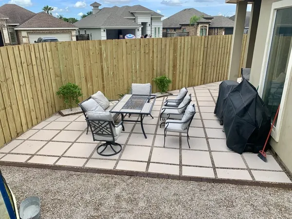 A back patio of large pale square pavers running up to a tall wooden privacy fence